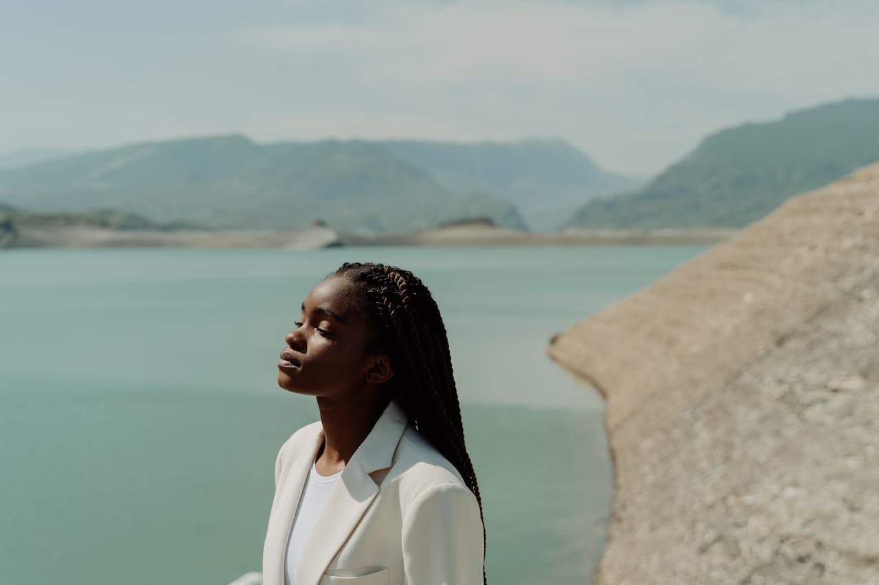 A fashionable woman in a white suit enjoys a peaceful moment by a tranquil lake.